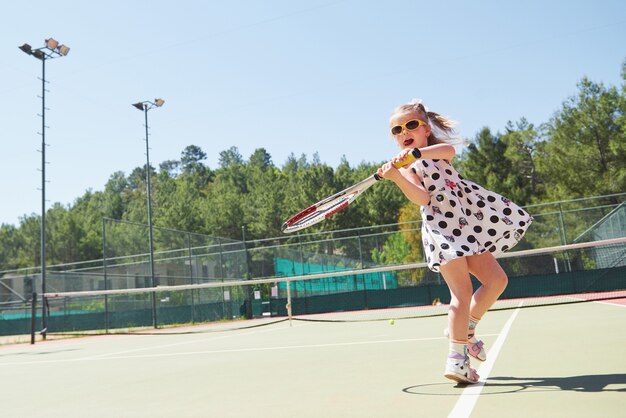 Счастливая маленькая девочка, играя в теннис. Летний спорт