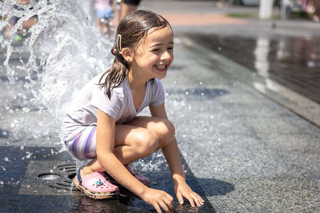 街の噴水の水しぶきの中で幸せな少女。