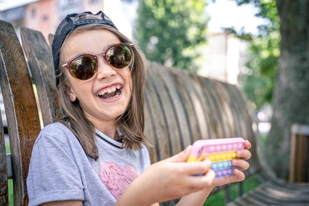 Free photo happy little girl in sunglasses with a smartphone in a trendy case pop it.