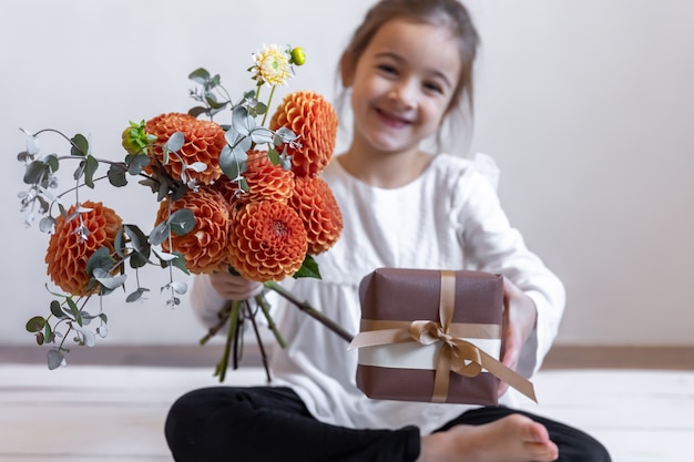 흐릿한 배경에 국화 꽃다발과 선물 상자를 가진 행복한 어린 소녀.