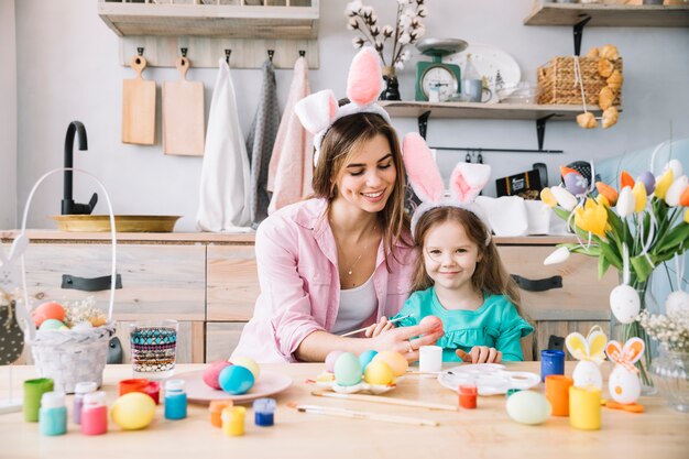 Happy little girl with mother painting eggs for Easter 