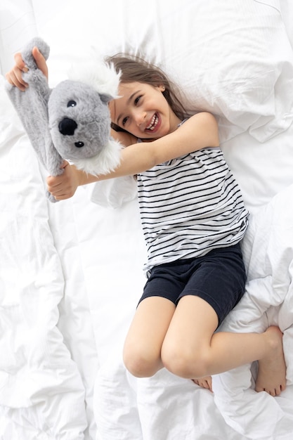 Happy little girl with soft toy koala in bed