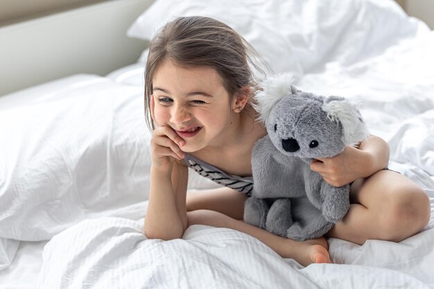 Счастливая маленькая девочка с мягкой игрушечной коалой в постели