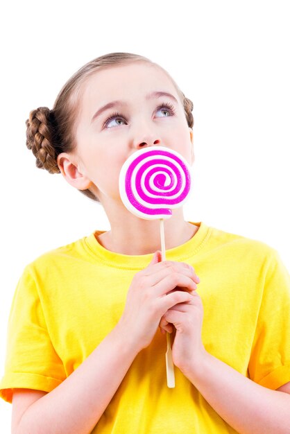 Happy little girl in yellow t-shirt eating colored candy - isolated on white.