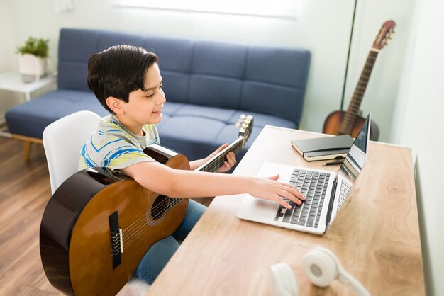 그의 온라인 음악 선생님과 이야기하면서 웃고 있는 행복한 어린 아이. 어쿠스틱 기타 연주를 배우기 위해 화상 통화를 하는 백인 소년