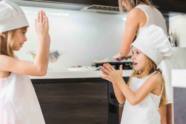 Sorelline felici in cappello da chef giocando in cucina