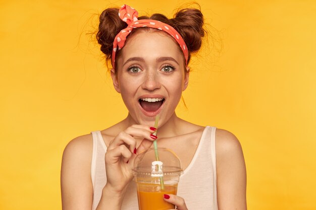 Happy looking red hair woman with buns. wearing white shirt and red doted hairband. looking excited and holding her juicy fresh