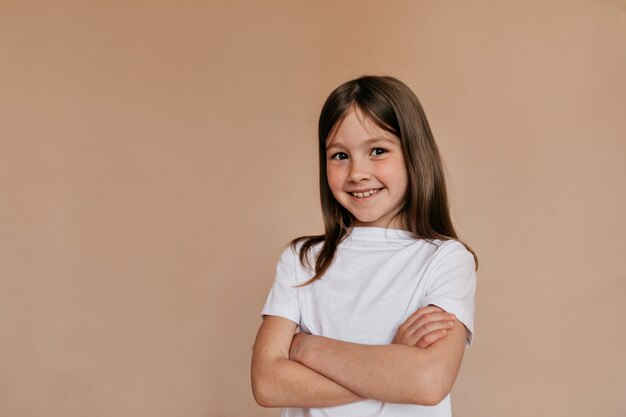 Happy lovable girl wearing white t-shirt posing over beige wall.