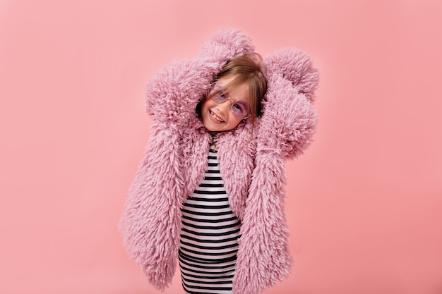 Foto gratuita felice bella ragazza che indossa elegante cappotto di pelliccia viola e occhiali rotondi alla moda in posa