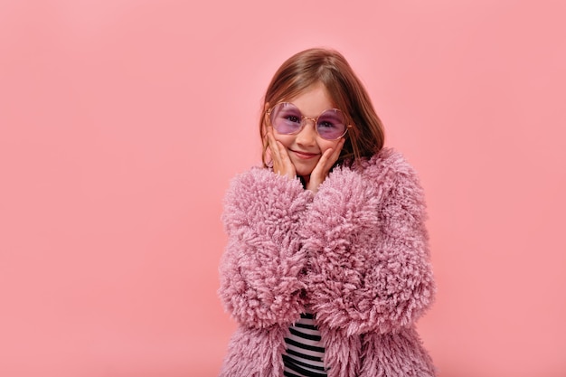 Free photo happy lovely little girl wearing round glasses and fur trendy coat posing