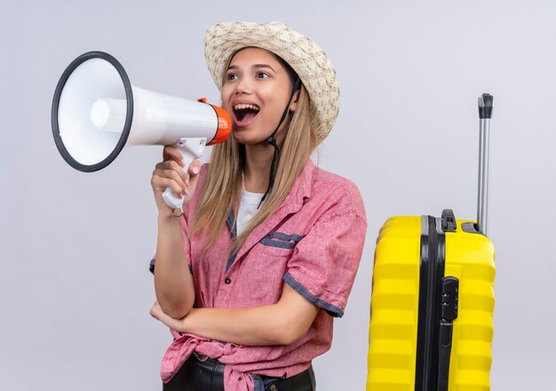 A happy lovely young woman wearing red shirt and sunhat speaking through megaphone on a white wall