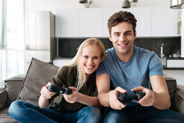 Happy lovers looking camera while playing video games at home