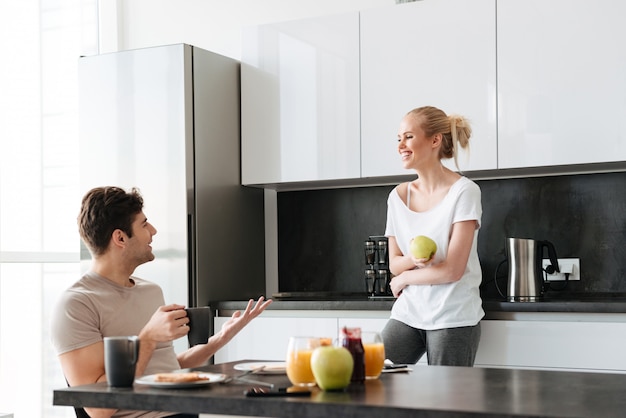 Happy lovers talking while sitting in kitchen in morning