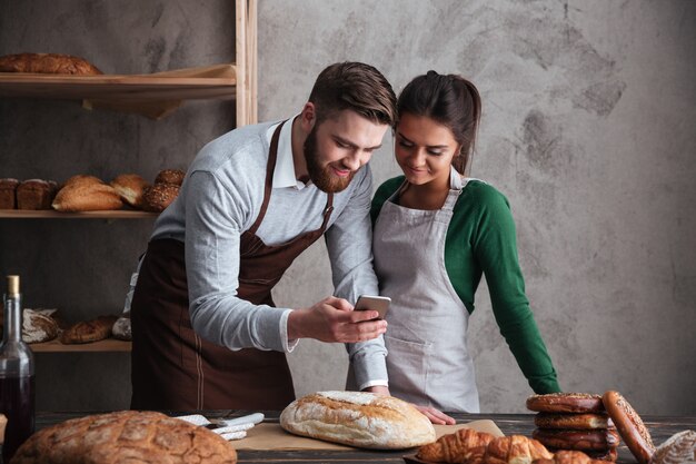 Счастливая любящая пара пекарей, стоя возле хлеба с телефоном