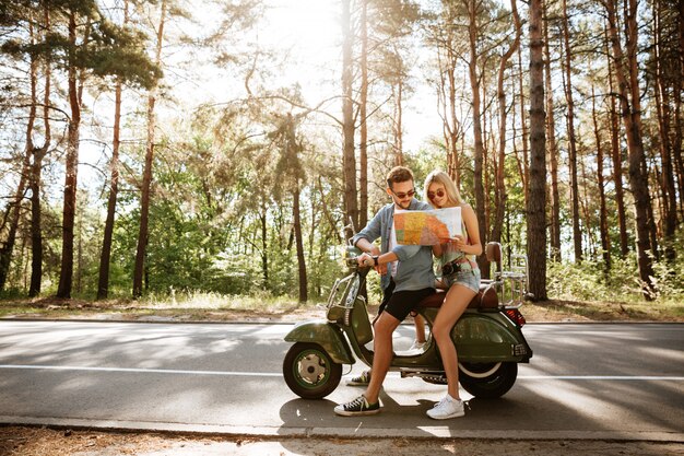 Счастливая любящая пара держит карту на открытом воздухе возле скутера