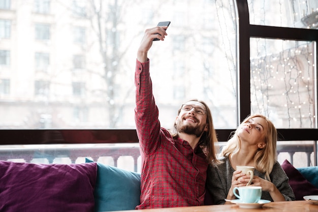 Happy loving couple sitting in cafe and make a selfie.