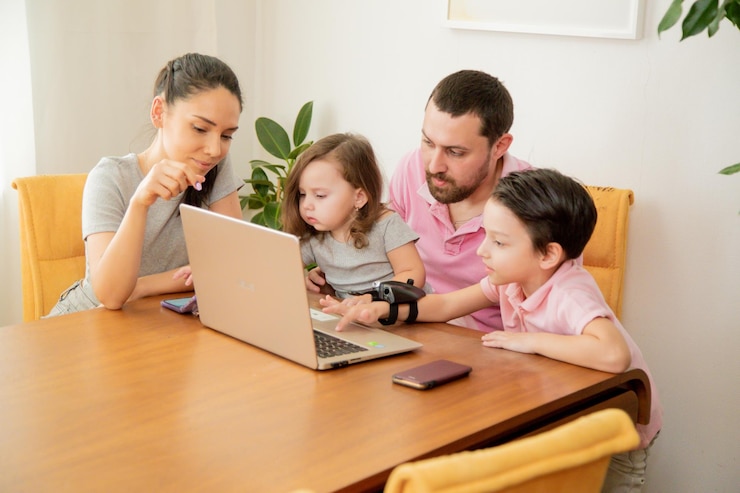Free Photo happy loving family couple parents and little cute children son and daughter sitting at the table together father working on laptop with busy face working at home concept