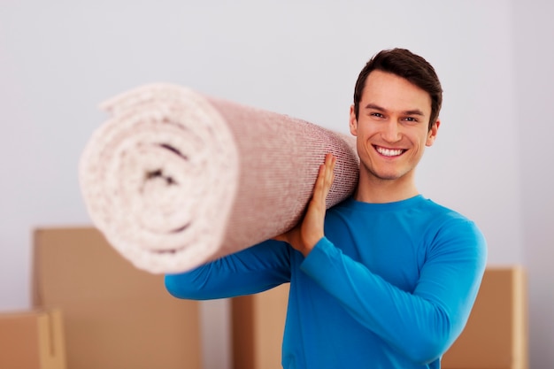 Happy male carrying a carpet in new home