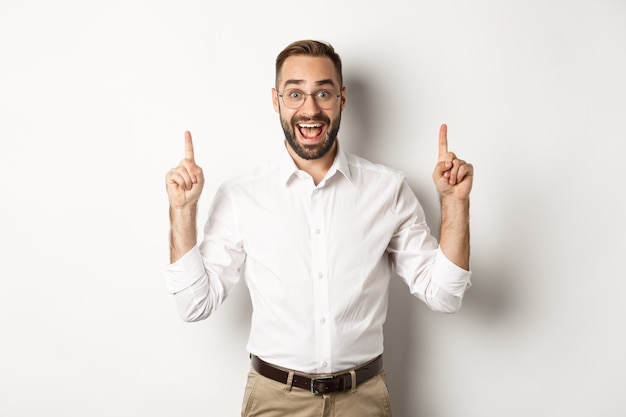 Happy male entrepreneur in business clothes, pointing fingers up and showing promo offer, standing