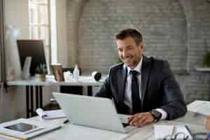 Foto gratuita imprenditore maschio felice che legge un'e-mail sul laptop mentre lavora in ufficio