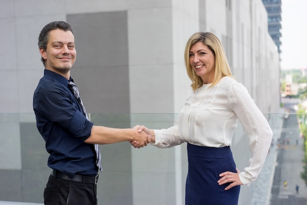 Happy male and female business partners shaking hands outdoors.