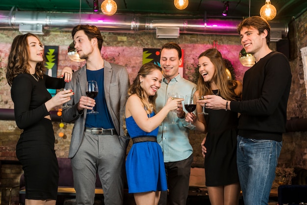 Счастливые друзья мужского и женского пола, пьющие и жарящие коктейли в баре