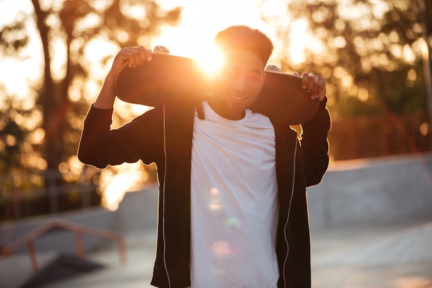 Happy male teenager guy holding skateboard on shoulders