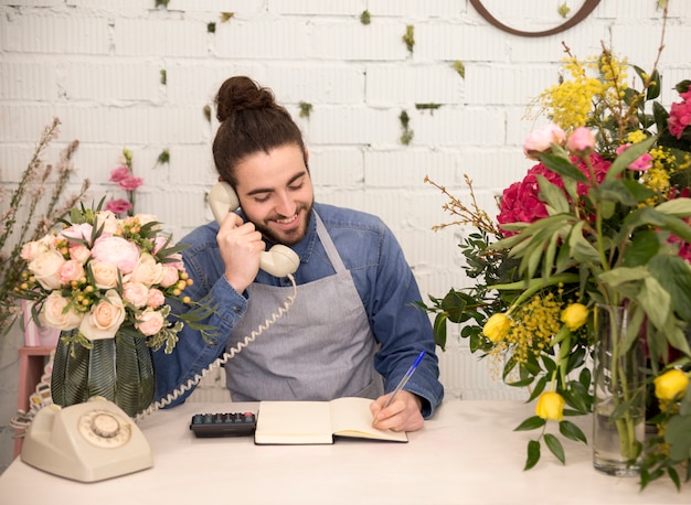 Happy male tourist taking the order on telephone in his florist shop