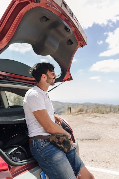 Foto gratuita viaggiatore maschio felice che si appoggia il tronco di automobile