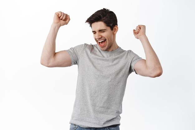 Happy man celebrating and having fun, dancing from success and satisfaction, standing satisfied against white background