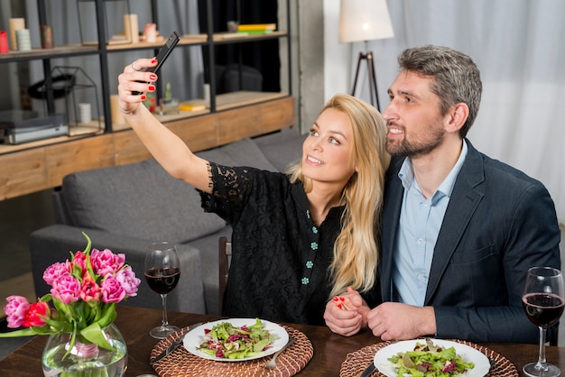 幸せな男とテーブルでスマートフォンでselfieを取っている陽気な女性