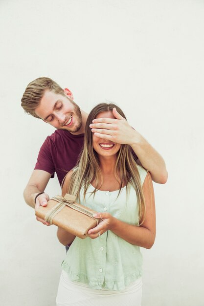 Happy man closing his girlfriend's eyes while giving surprise gift