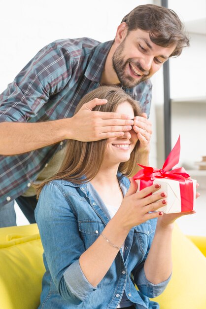 誕生日プレゼントをしている彼のガールフレンドの目を覆う幸せな男