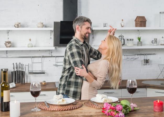 Happy man dancing with blond woman near table in kitchen