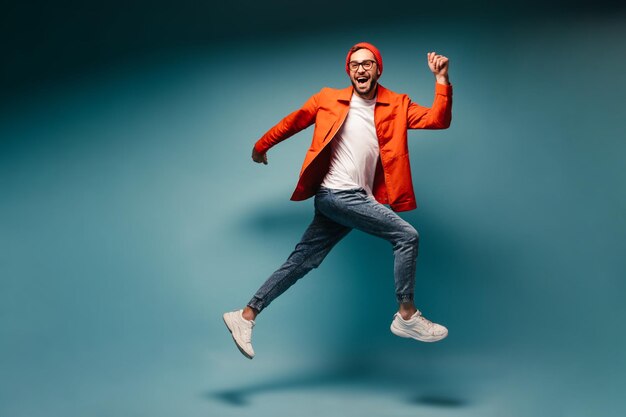 Happy man dressed in jeans and orange jacket runs on blue background