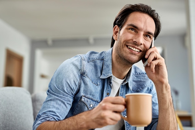 Uomo felice che beve caffè e comunica tramite telefono cellulare a casa