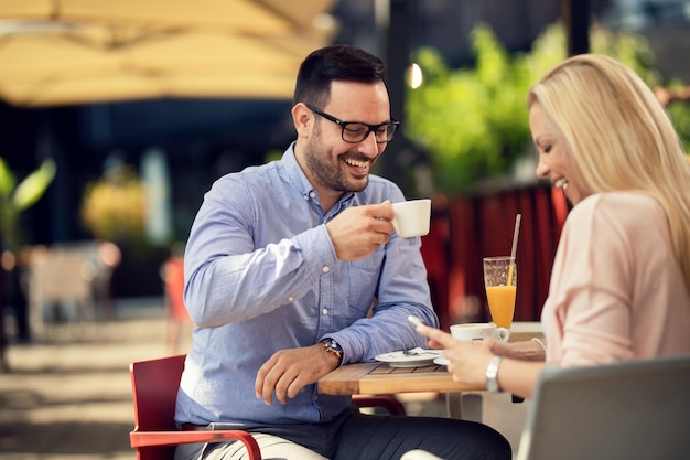 彼女がカフェで携帯電話を使用している間、コーヒーを飲み、彼のガールフレンドと楽しんでいる幸せな男