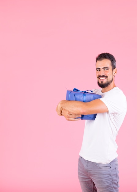 Foto gratuita uomo felice che abbraccia il contenitore di regalo contro il contesto rosa