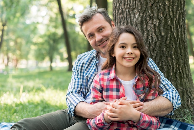 Счастливый человек, обнимая свою дочь, сидя в парке