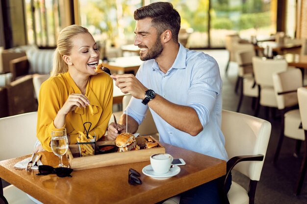 Счастливый мужчина кормит свою девушку во время обеда в ресторане