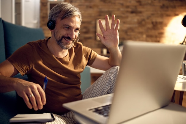 Happy man greeting someone during video call while working at night at home