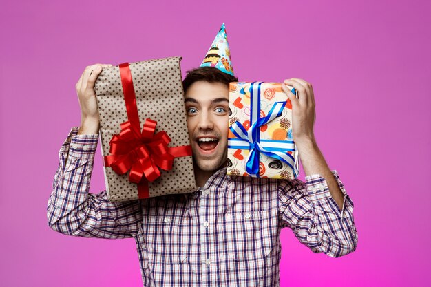 Happy man holding birthday gifts in boxes over purple wall.