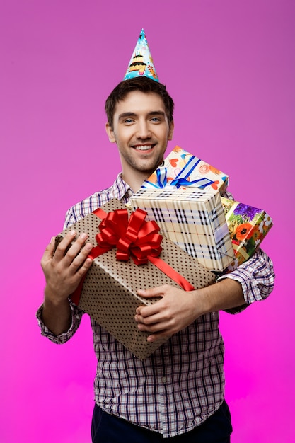 Счастливый человек держа подарки на день рождения в коробках над фиолетовой стеной.