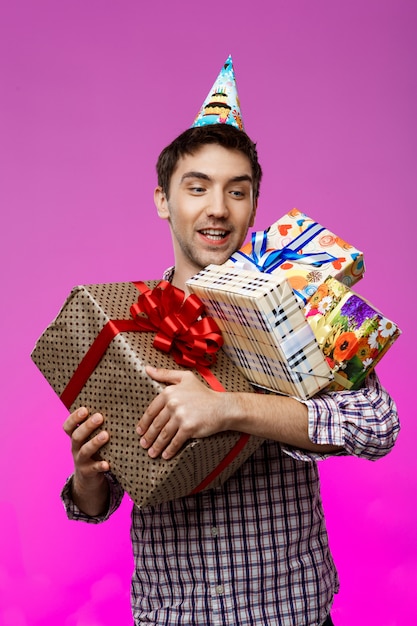 Happy man holding birthday gifts in boxes over purple wall.