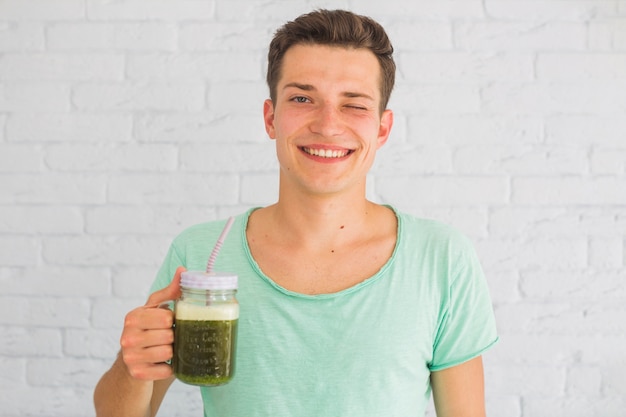 Happy man holding blended green smoothies in jar winking