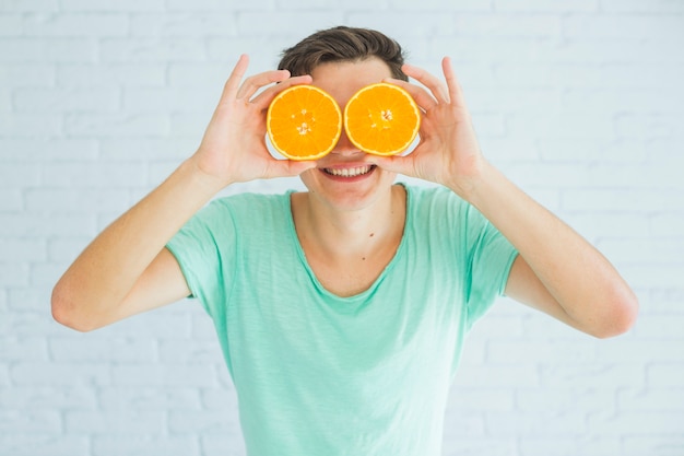 Happy man holding halved ripe oranges in front of his eyes