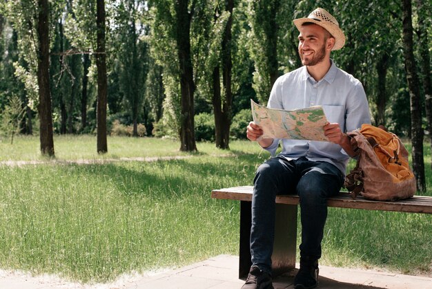 Happy man holding map sitting on bench with backpack