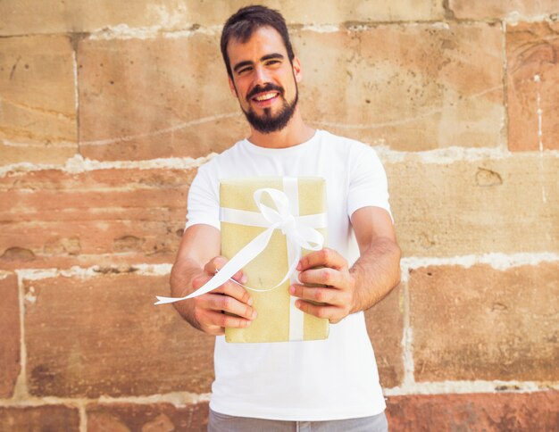 Happy man holding present in front of wall