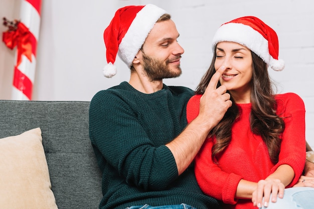 Happy man holding woman's nose on sofa