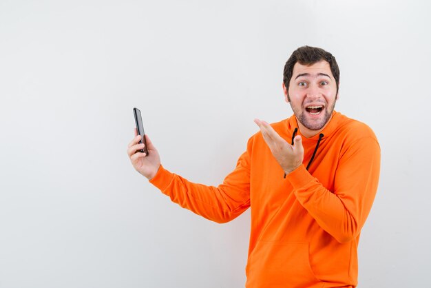 Счастливый человек показывает свой мобильный телефон рукой на белом фоне
